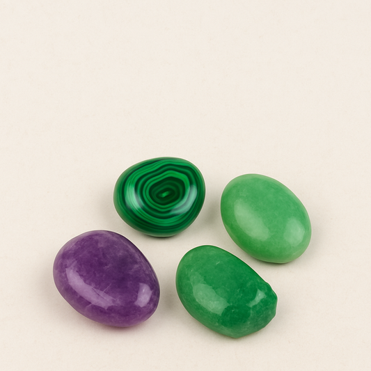 Quatre pierres naturelles polies – améthyste violette, malachite verte rayée, jade vert doux et émeraude brute – disposées sur un fond beige clair